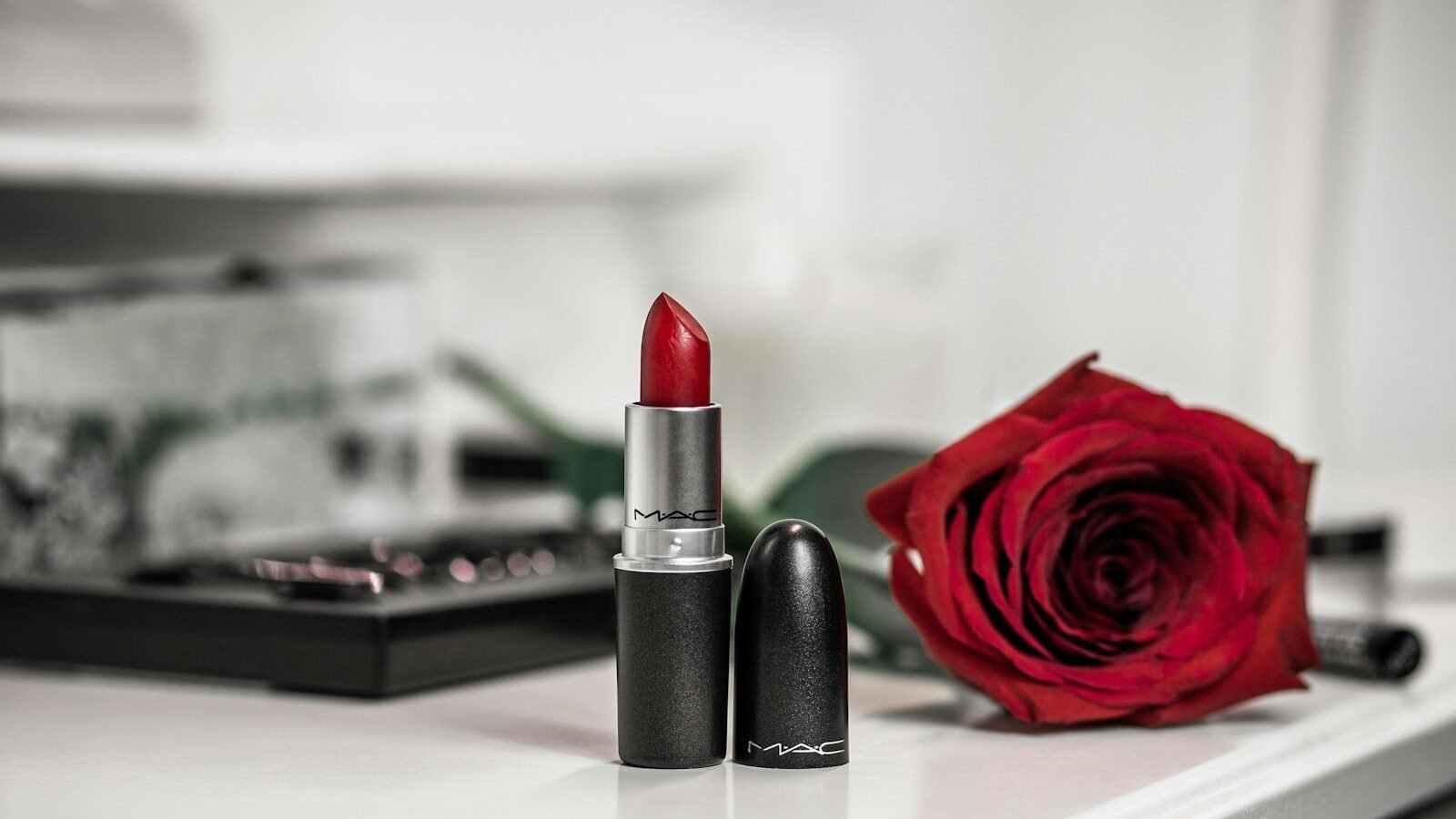 a close up of a lipstick and a rose on a table