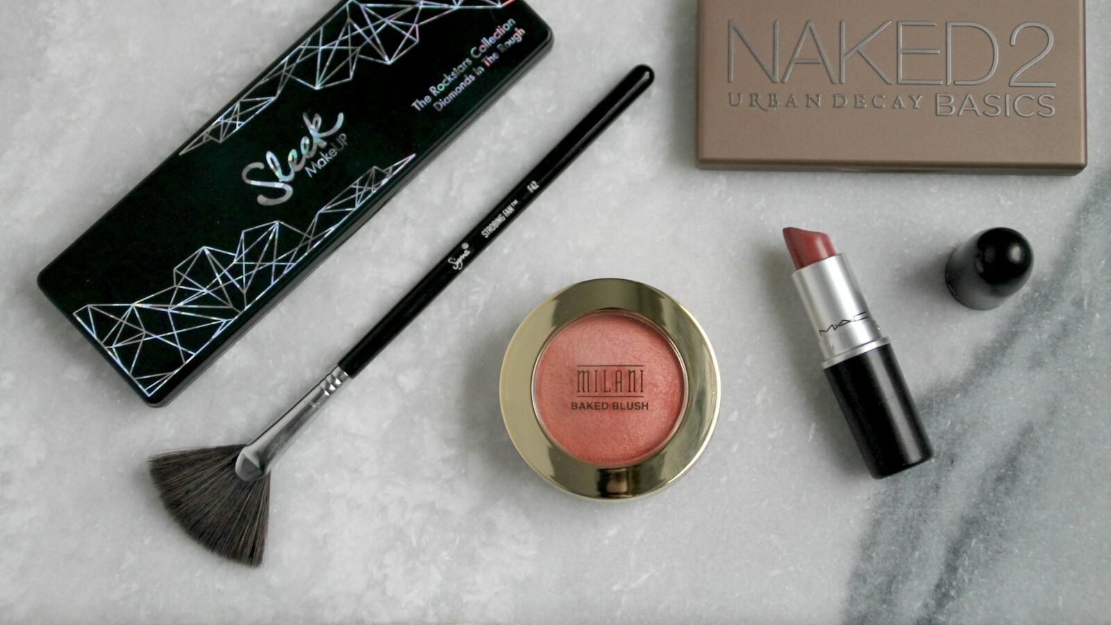black makeup brush, red lipstick, and blush foundation powder displaying on the marble table.